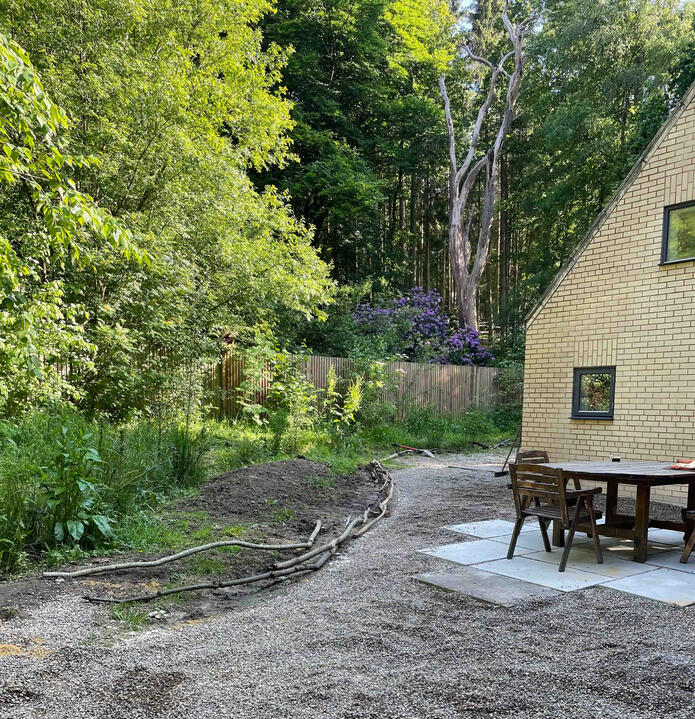 Outdoor seating area beside a woodland garden in the Lab Garden, Ascot, featuring permeable gravel surfacing and natural log edging — blending sustainable design with nature-based living.